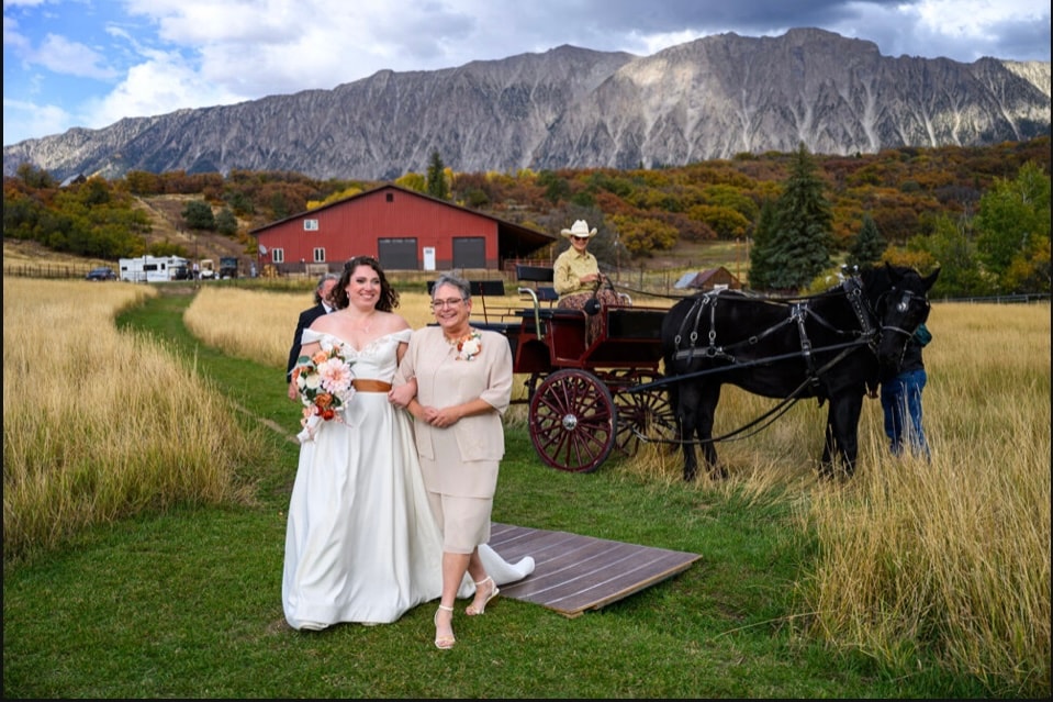 Bride walking the aisle with family beside the horse-drawn carriage, red barn and Ragged Mountain in the background