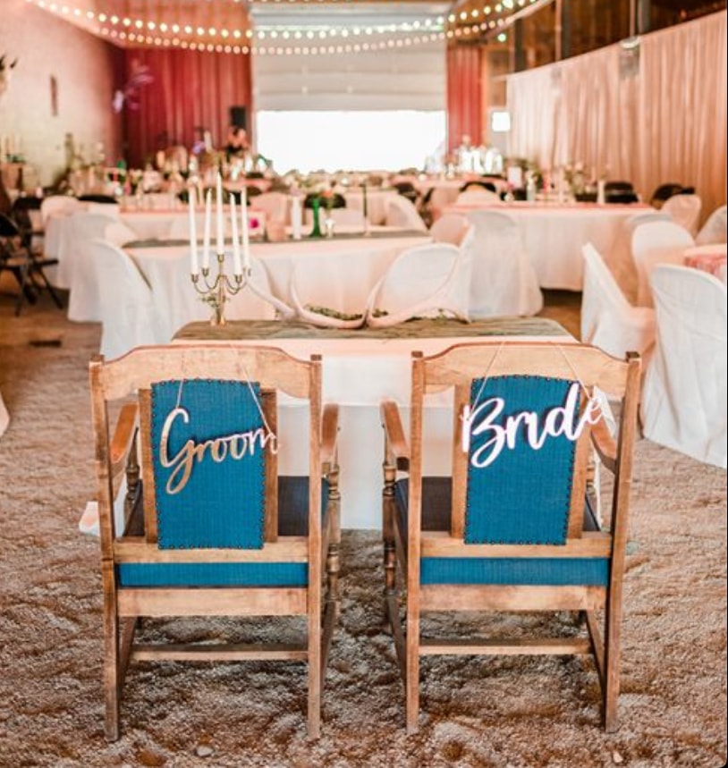 Bride and Groom chairs with reception tables and string lights in the barn