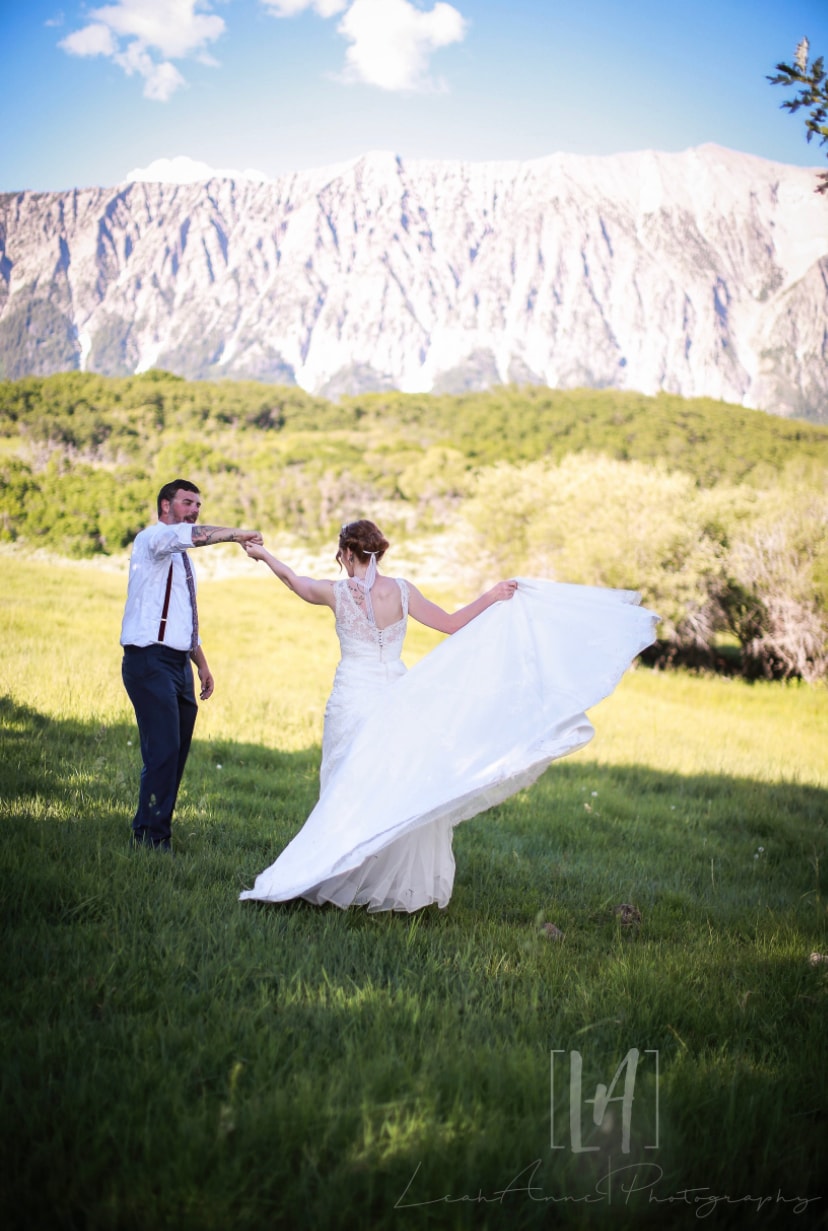 Groom spinning bride as her dress flows in the mountain meadow