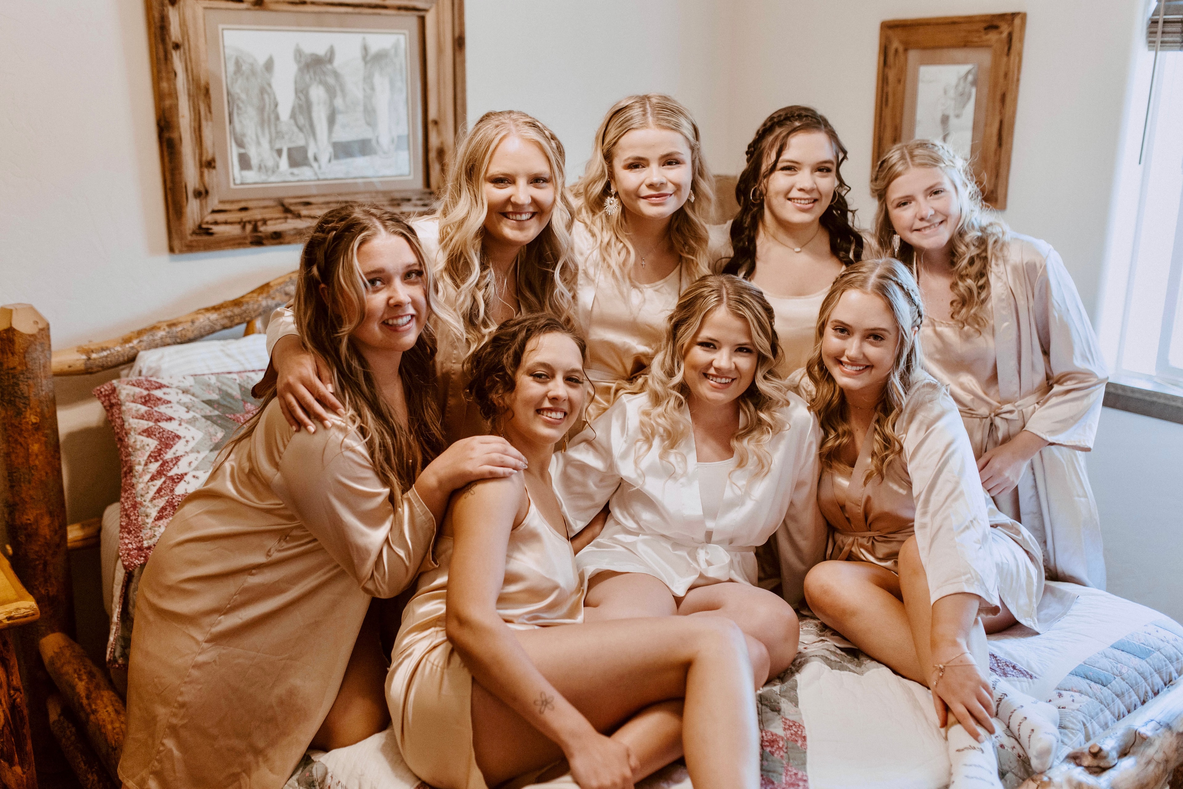 Bride and bridesmaids in satin robes laughing together while getting ready in the rustic cabin