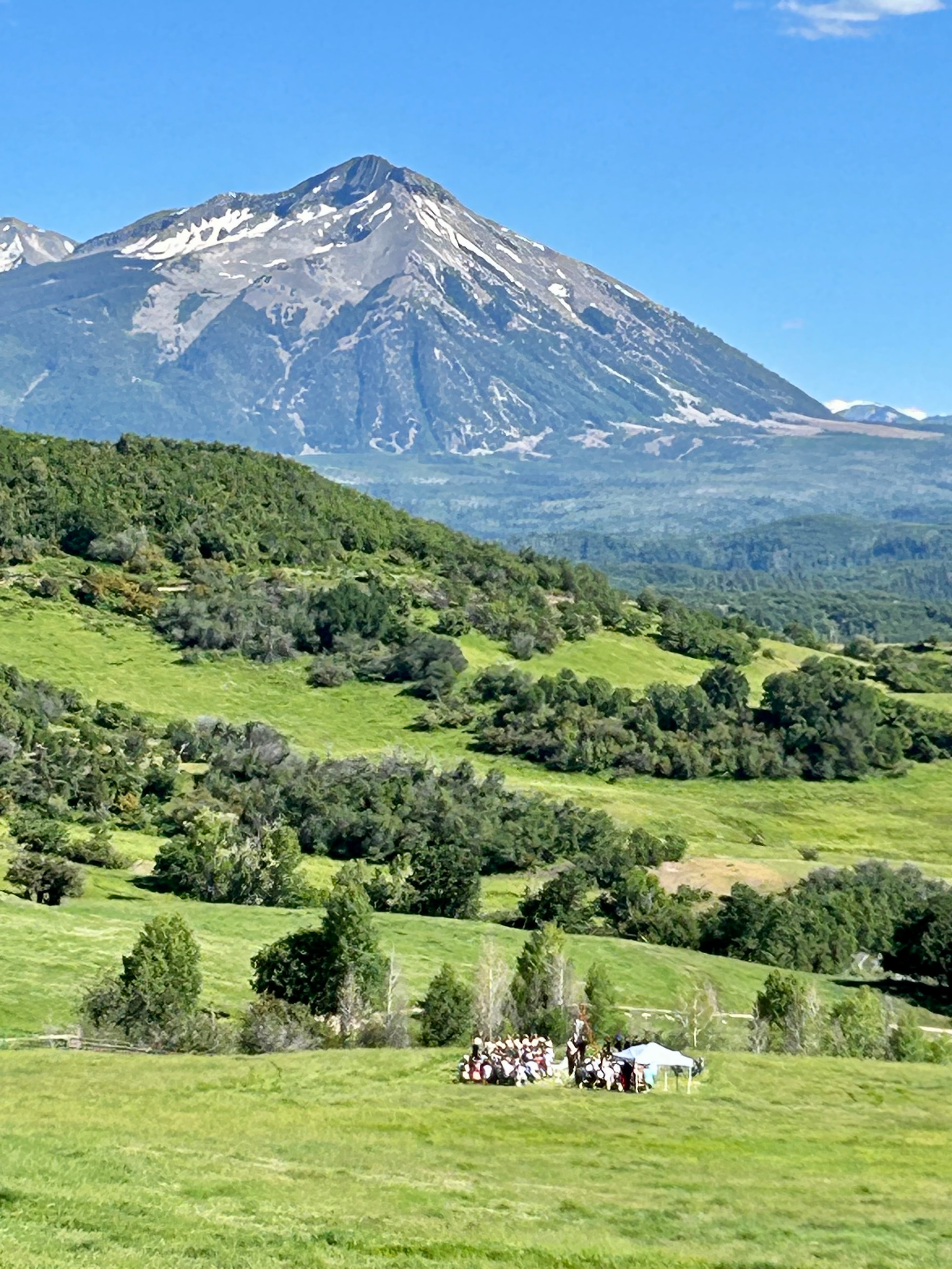Wide view of the outdoor ceremony nestled in the green meadow with Ragged Mountain's snow-capped peak towering above
