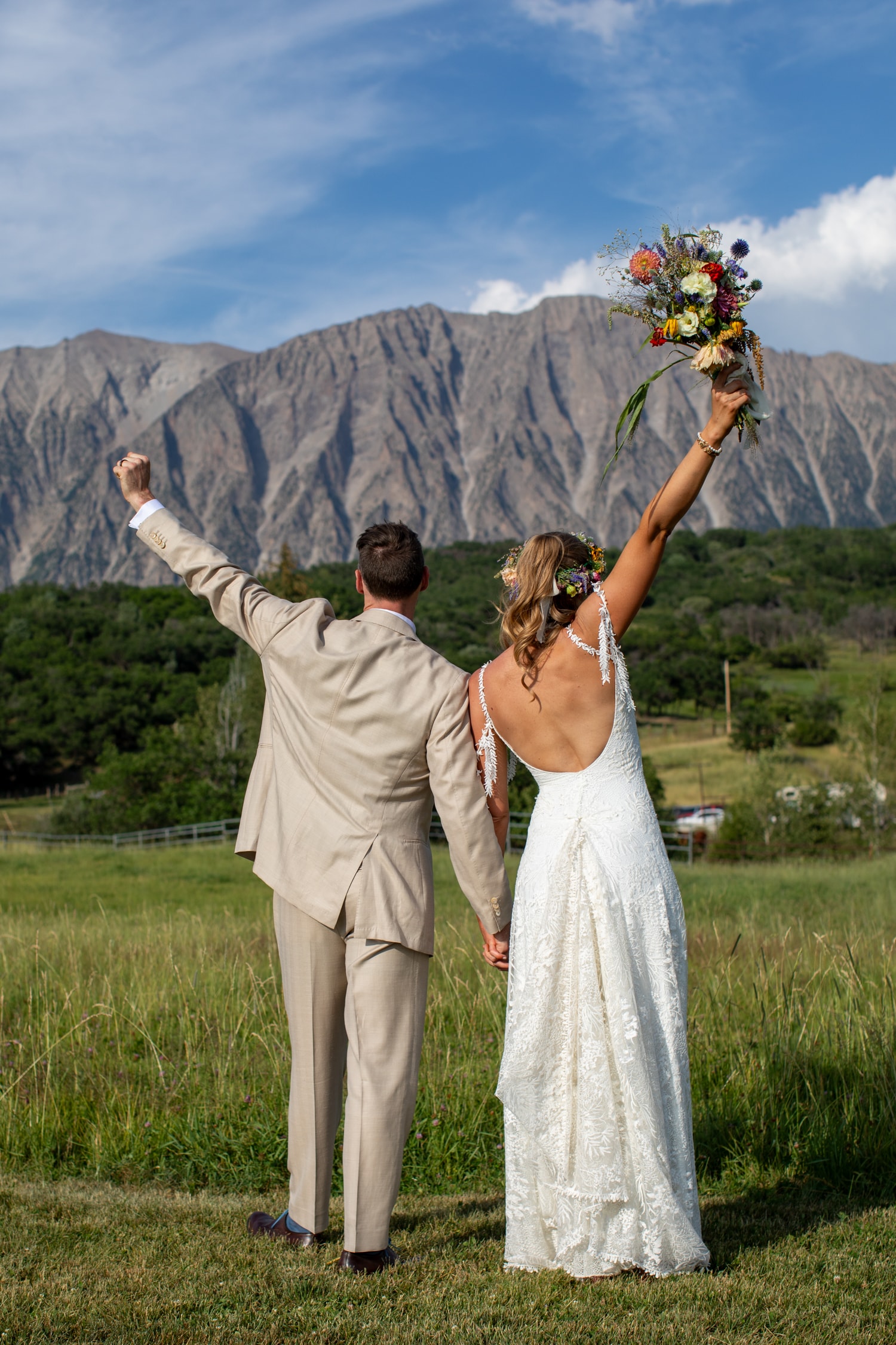 Bride and groom facing Ragged Mountain with arms raised in celebration, bouquet held high