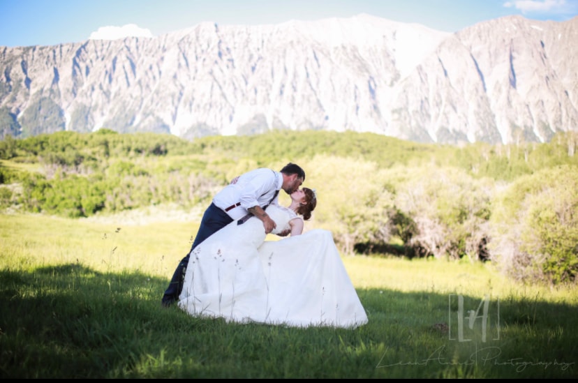 Groom dipping bride for a kiss in the green meadow with Ragged Mountain behind them