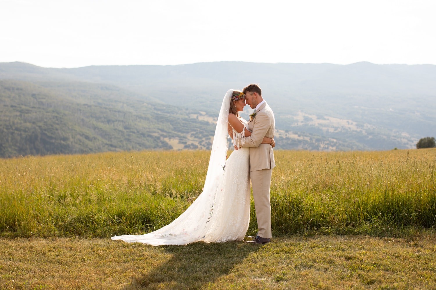 Bride and groom touching foreheads in a quiet moment in the golden meadow with sweeping mountain valley views