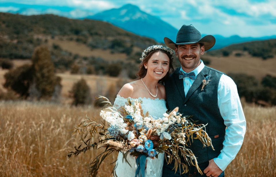 Bride and groom portrait in golden field with mountain backdrop