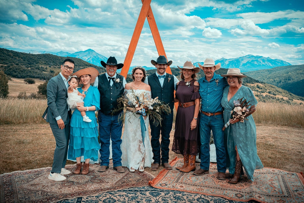 Wedding party and family gathered under the wooden ceremony arch with panoramic mountain views stretching behind them