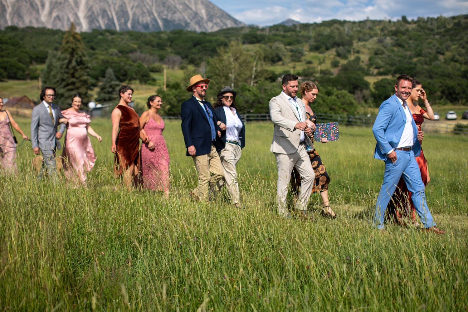 Wedding guests and wedding party walking through the tall grass meadow with Ragged Mountain rising behind them